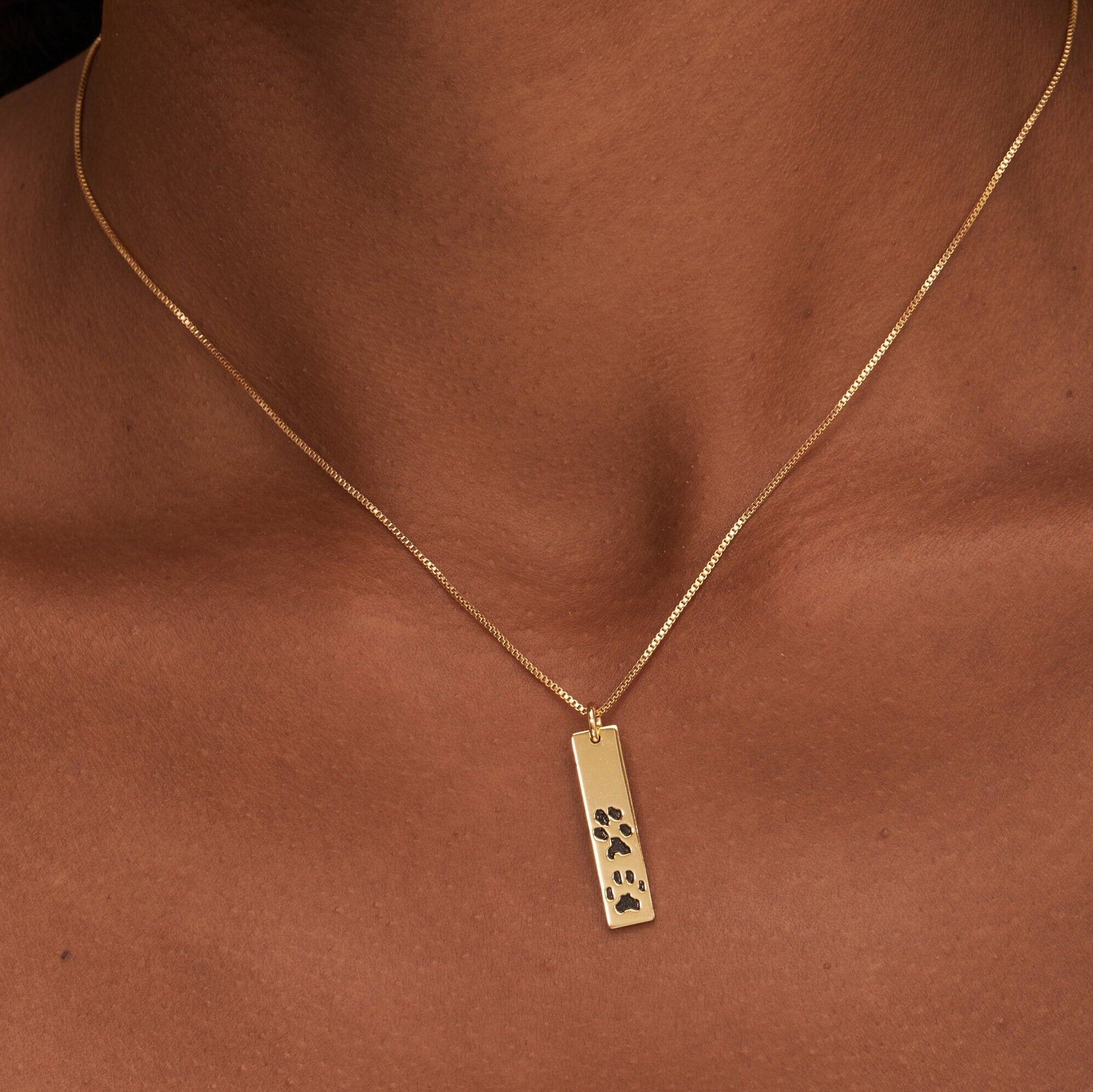 Gold necklace with a pendant featuring paw prints on a brown background