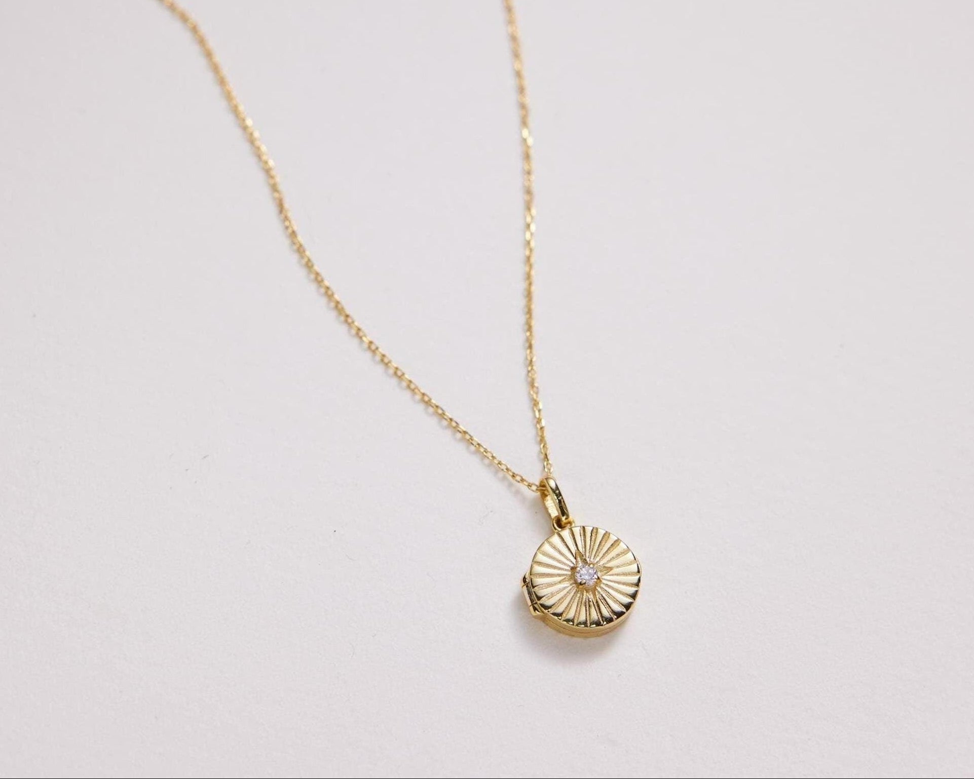 Gold necklace with a round pendant on a light gray background