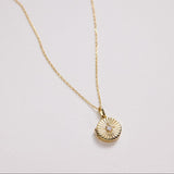 Gold necklace with a round pendant on a light gray background