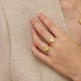 A close-up of a person's hand wearing two gold-colored rings with seashell designs.