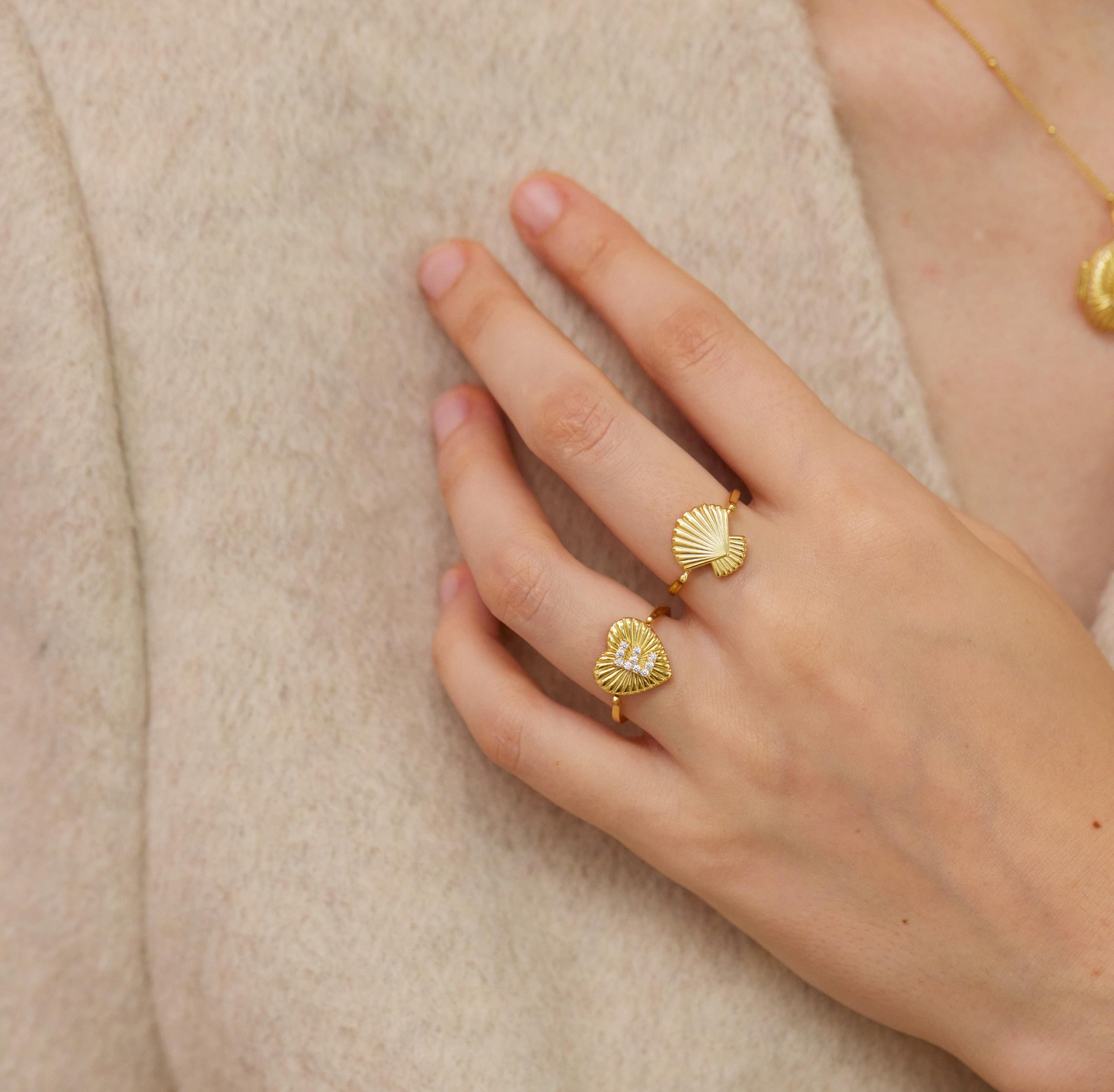 A close-up of a person's hand wearing two gold-colored rings with seashell designs.