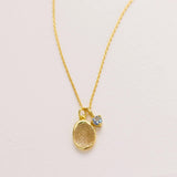 A gold necklace with a small pendant featuring a textured design.