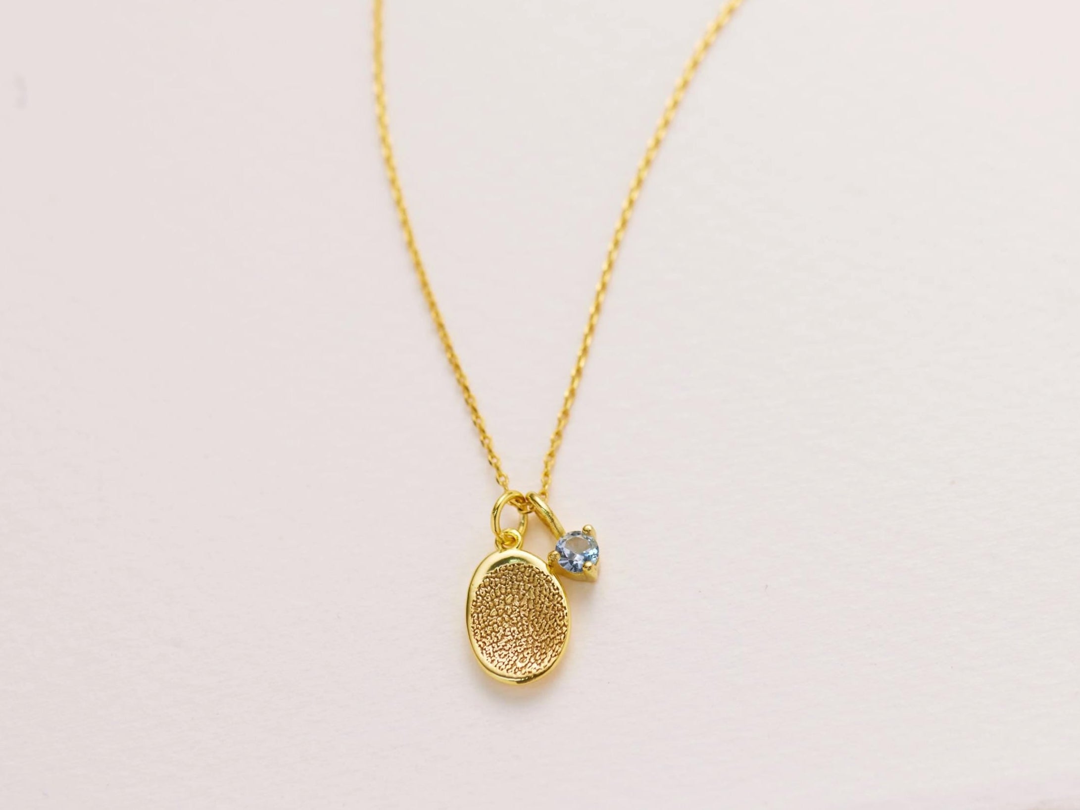 A gold necklace with a small pendant featuring a textured design.