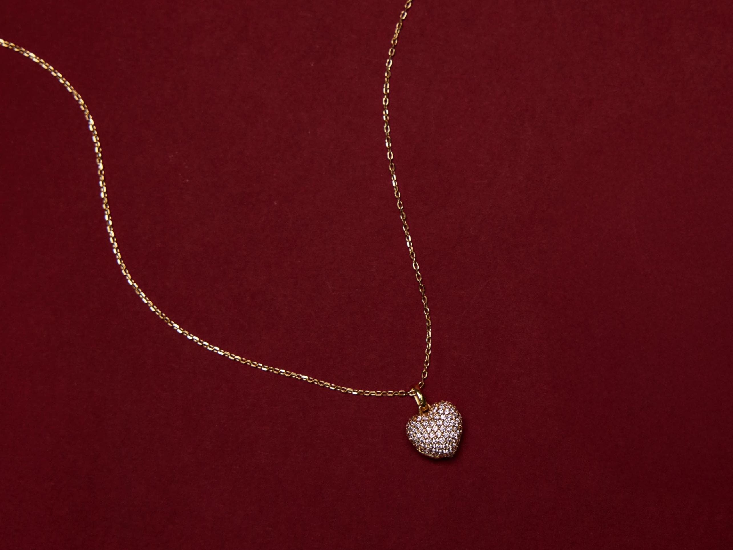 Gold necklace with a heart-shaped pendant on a red background