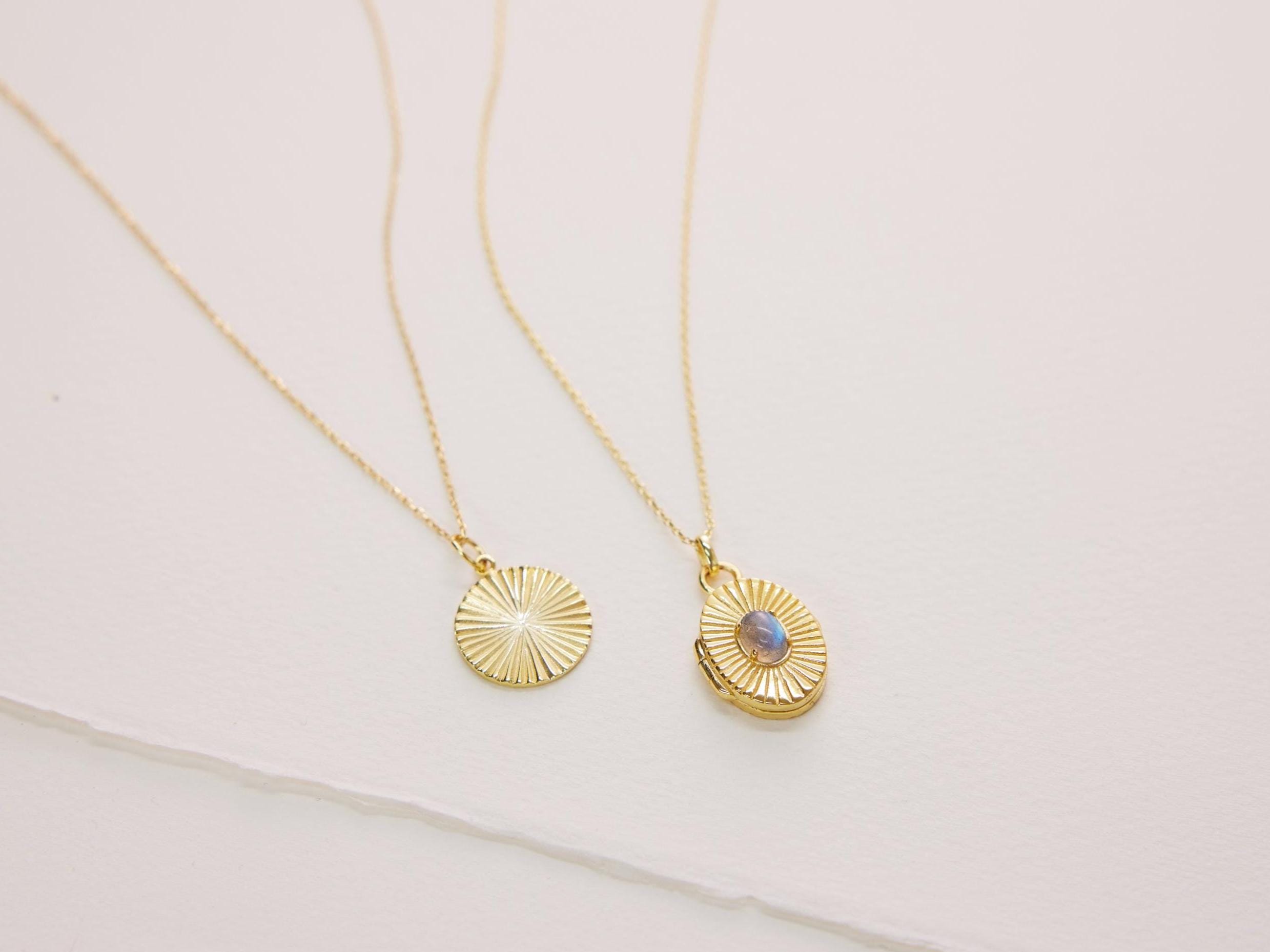 Two gold necklaces with circular pendants on a light background