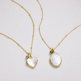 Two gold necklaces with heart and oval pendants on a light gray background