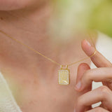 A close-up of a person's neck and hand wearing a gold necklace with a pendant.