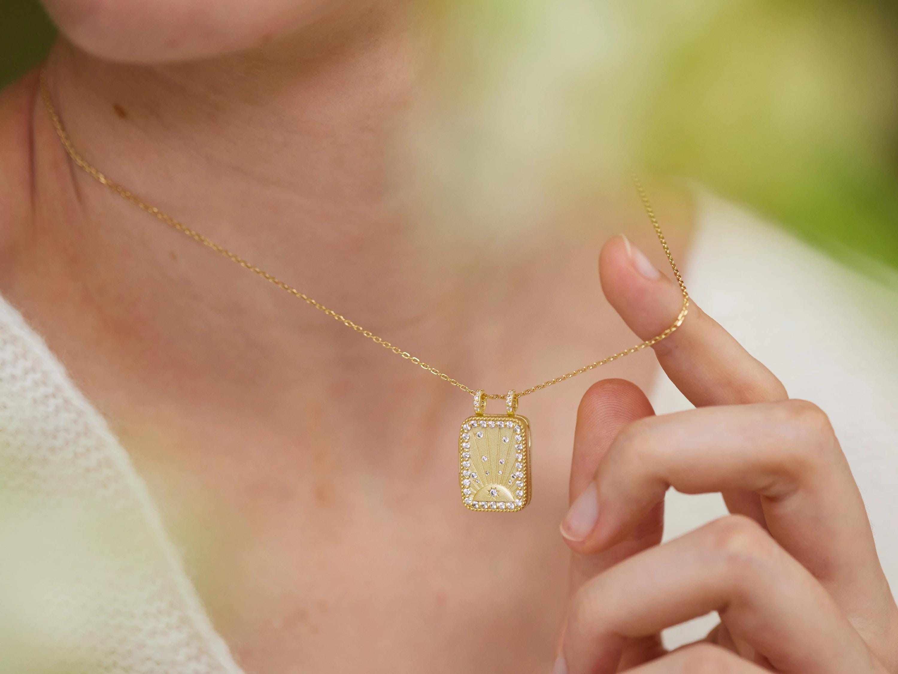 A close-up of a person's neck and hand wearing a gold necklace with a pendant.