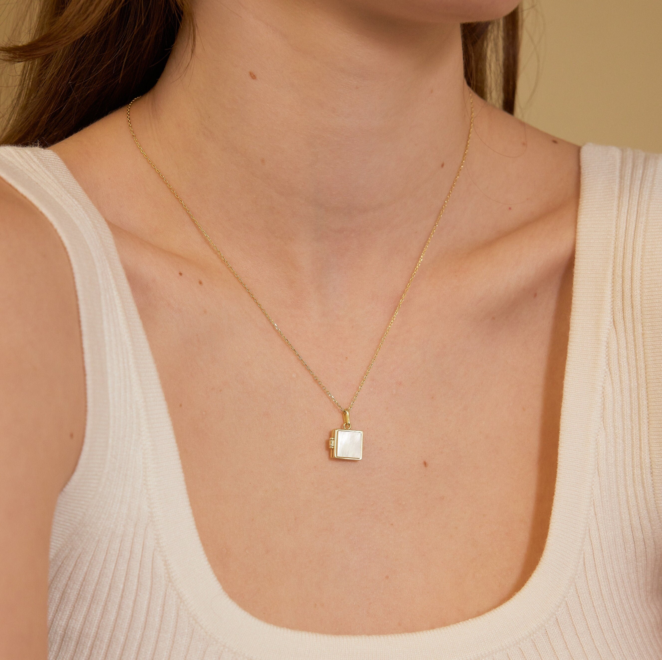 Gold necklace with a square pendant worn by a person in a beige top.