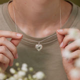 A person is holding a silver necklace with a heart-shaped pendant that has the letter &quot;M&quot; engraved on it.