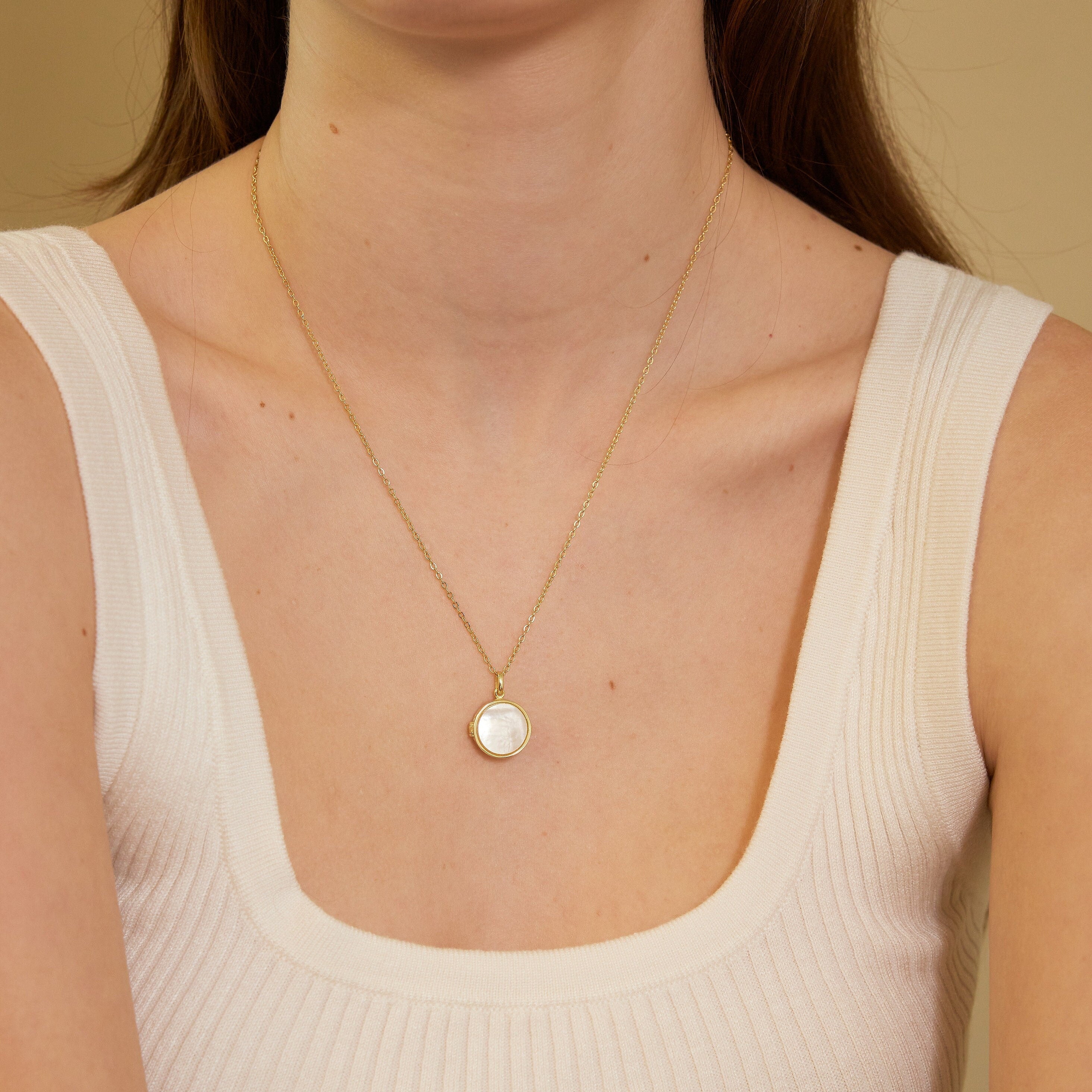 Gold necklace with a pendant worn by a person in a beige top against a neutral background