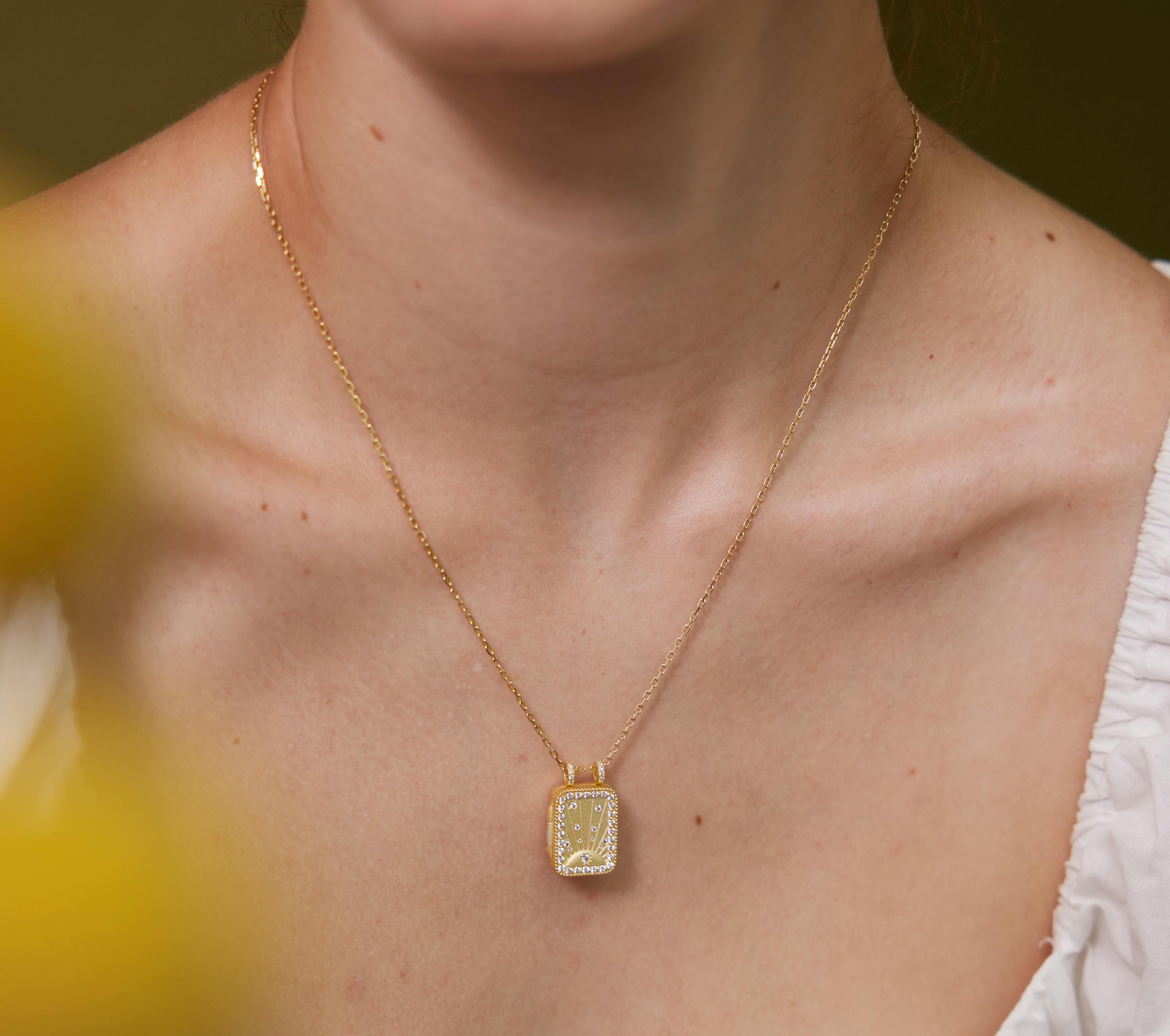 A gold necklace with a square pendant is worn around a person's neck.