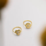 Two gold rings with heart-shaped designs and letters on them are placed on a white surface.