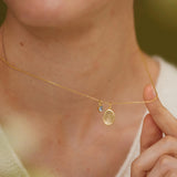 A close-up of a person's neck and chest wearing a gold necklace with a small pendant.