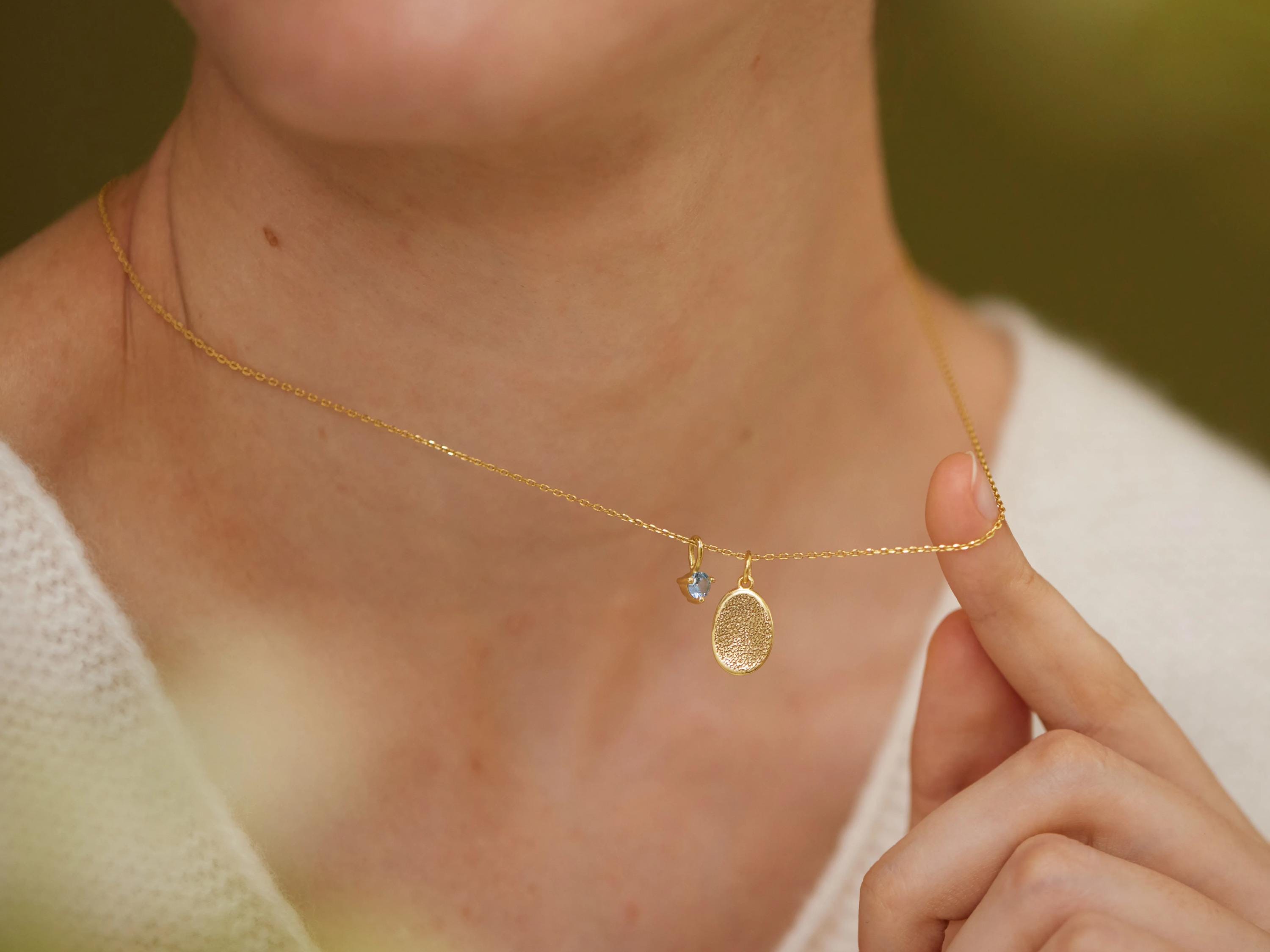 A close-up of a person's neck and chest wearing a gold necklace with a small pendant.