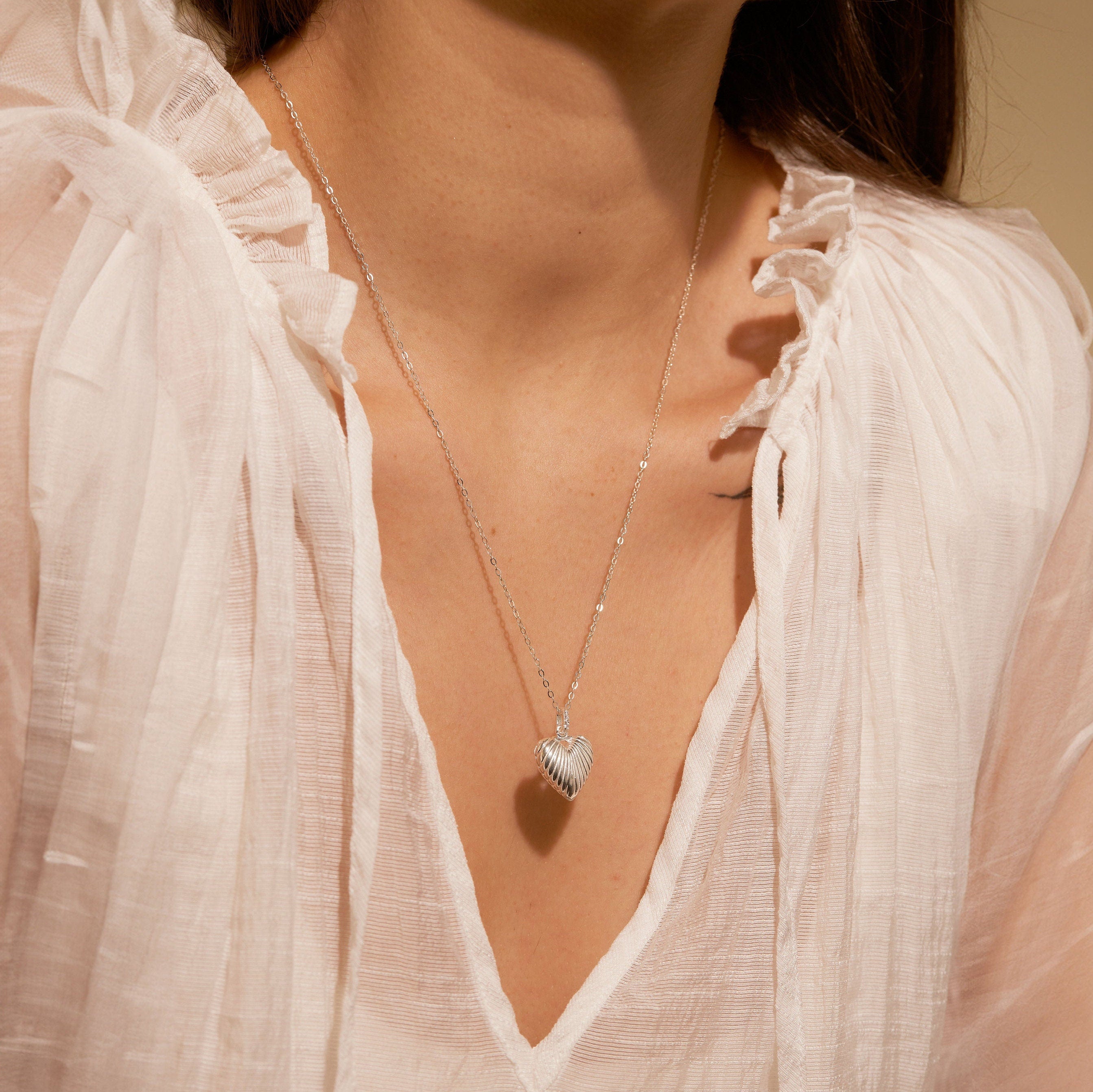 Necklace with a heart pendant worn by a person in a white blouse.