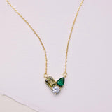 Gold necklace with green gemstone pendant on a light pink background