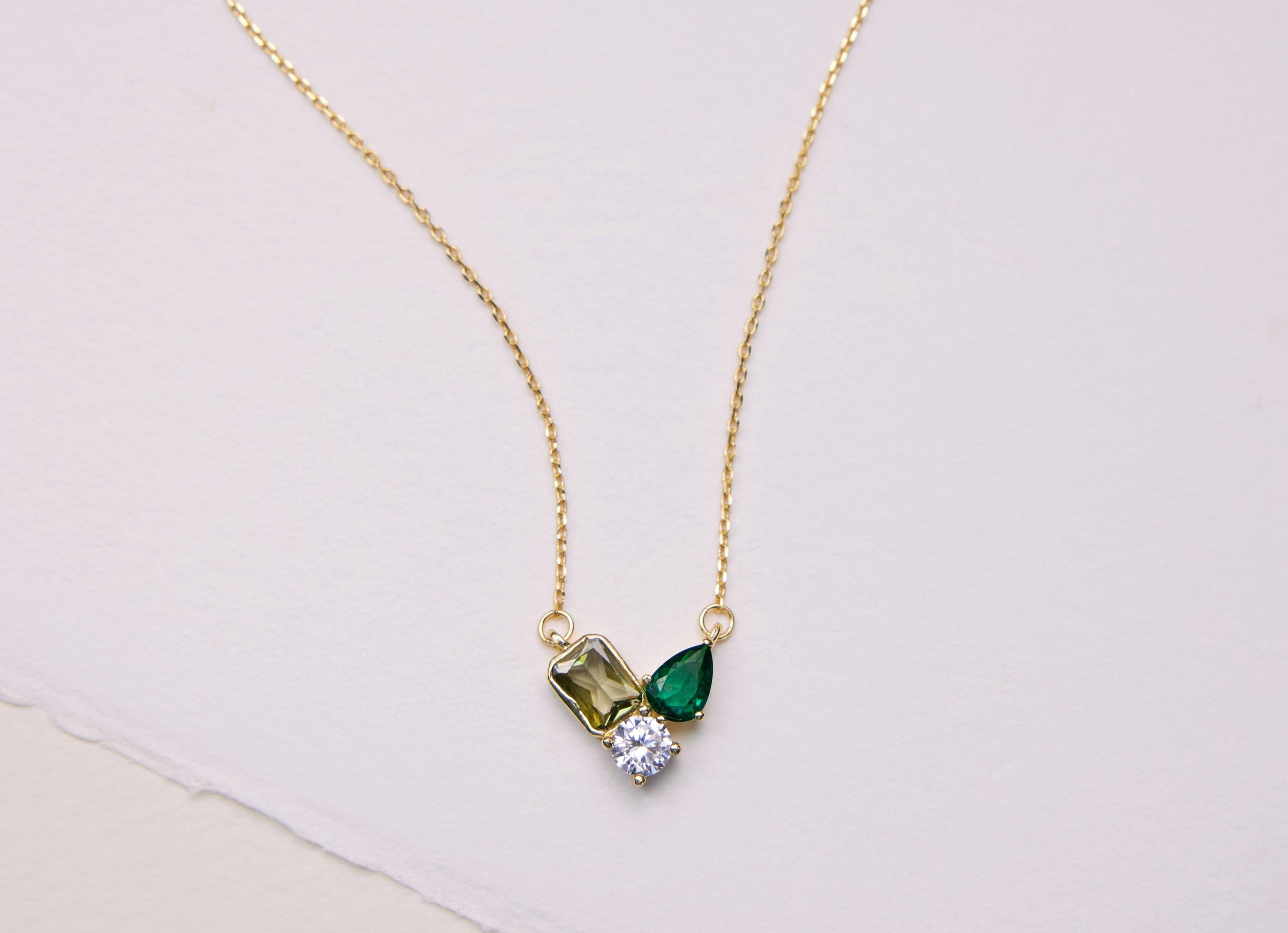 Gold necklace with green gemstone pendant on a light pink background