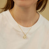 May include: A gold chain necklace with a small, round pendant. The pendant has a white background and a gold design in the center.