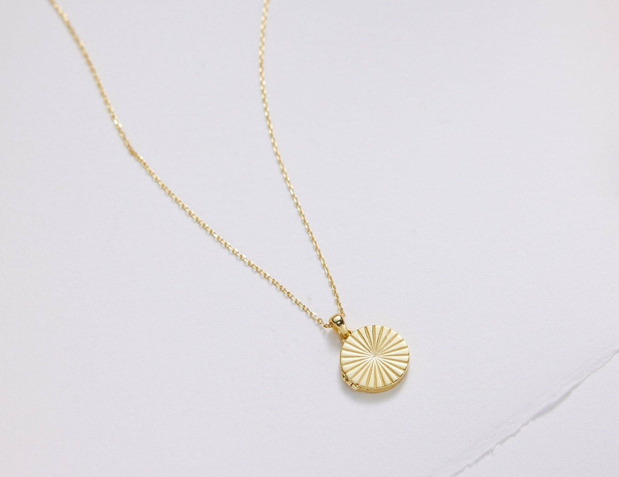 Gold necklace with a round pendant on a light gray background
