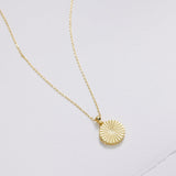 Gold necklace with a round pendant on a light gray background