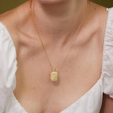 A close-up of a woman wearing a gold necklace with a pendant.