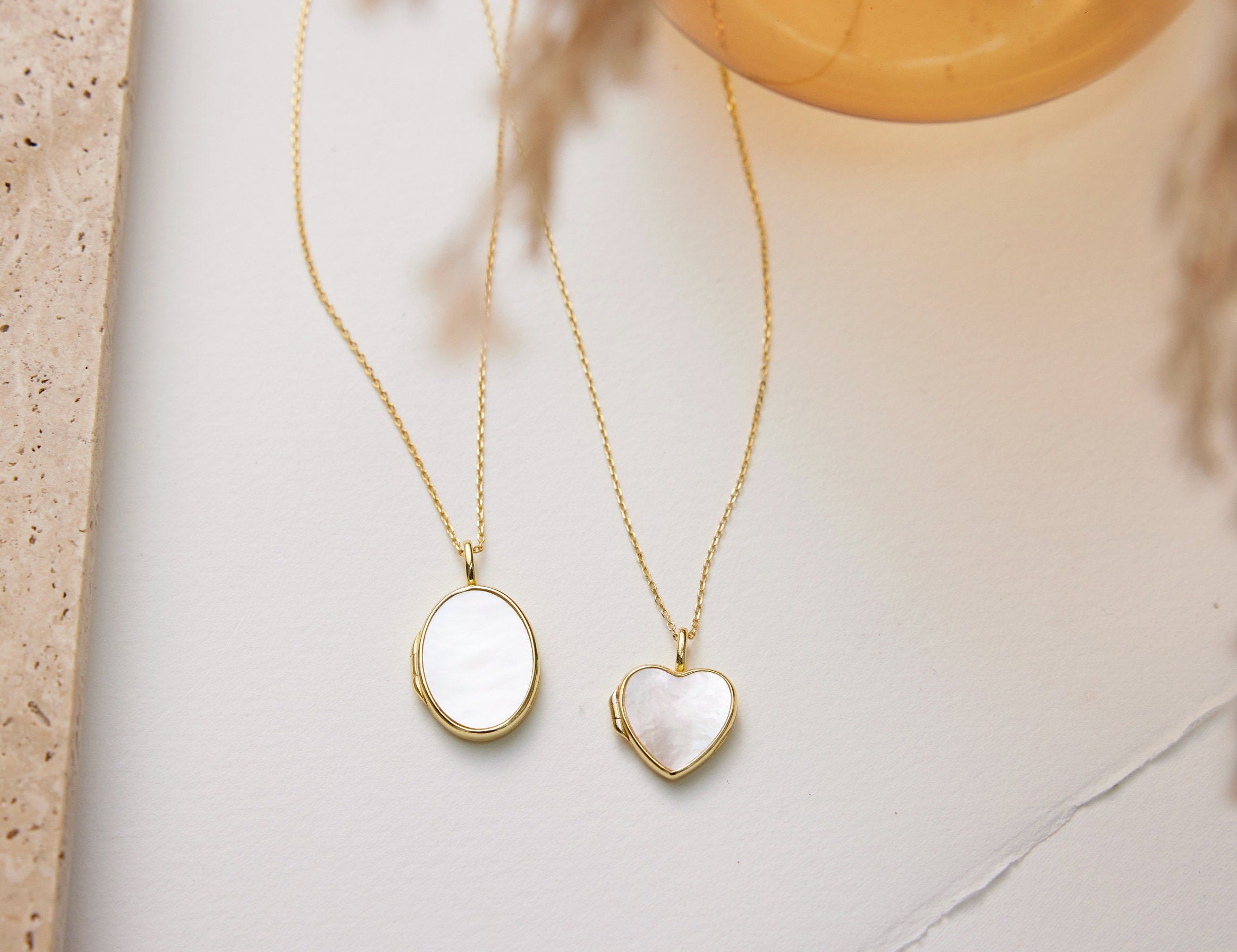 Two gold necklaces with heart-shaped pendants on a neutral background