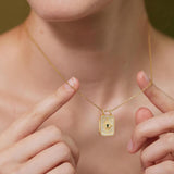 A close-up of a person&#39;s hand holding a gold necklace with a pendant, wearing a white blouse.