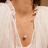 Close-up of a necklace with a shell pendant worn by a person in a white blouse.