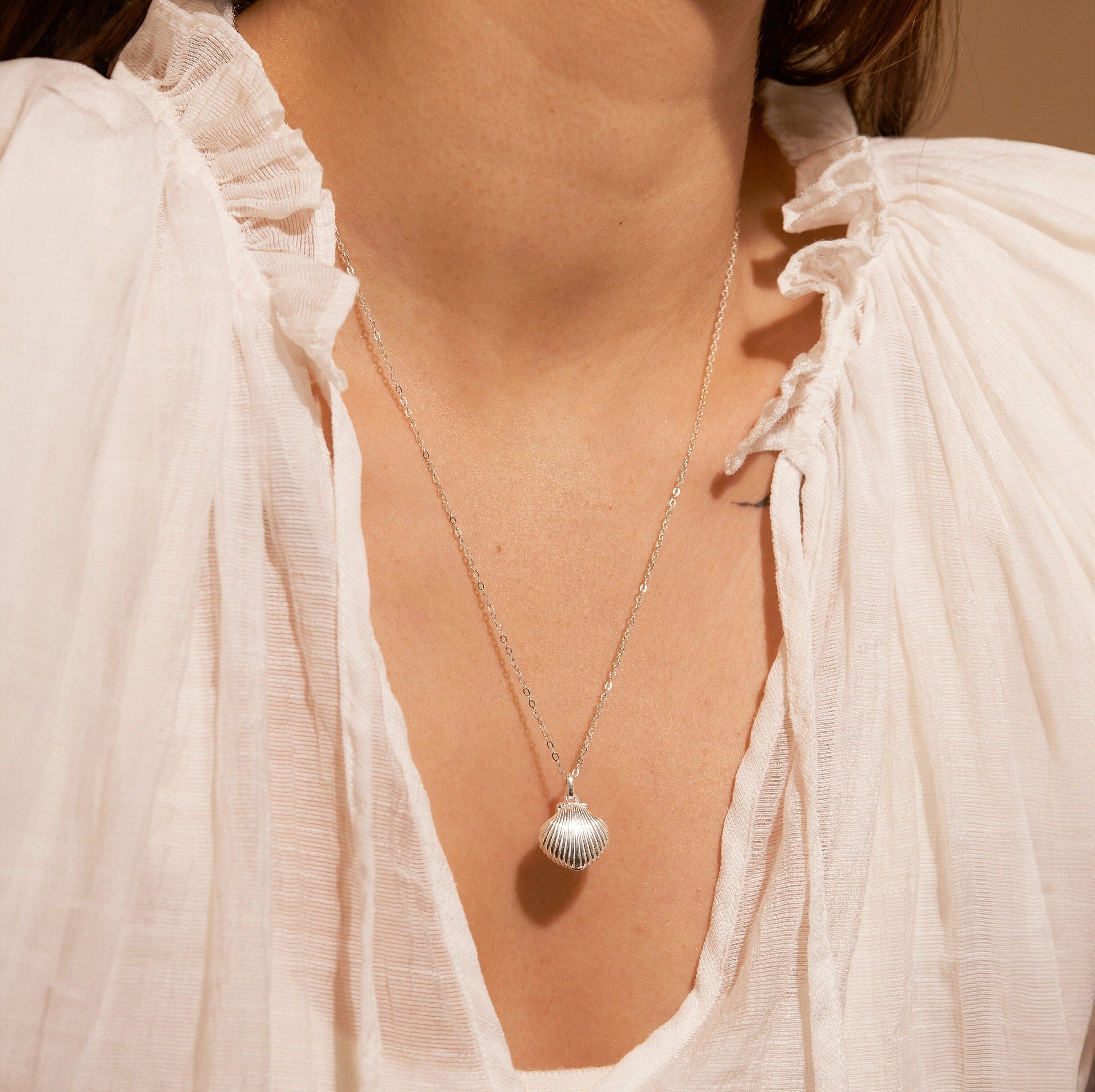 Close-up of a necklace with a shell pendant worn by a person in a white blouse.