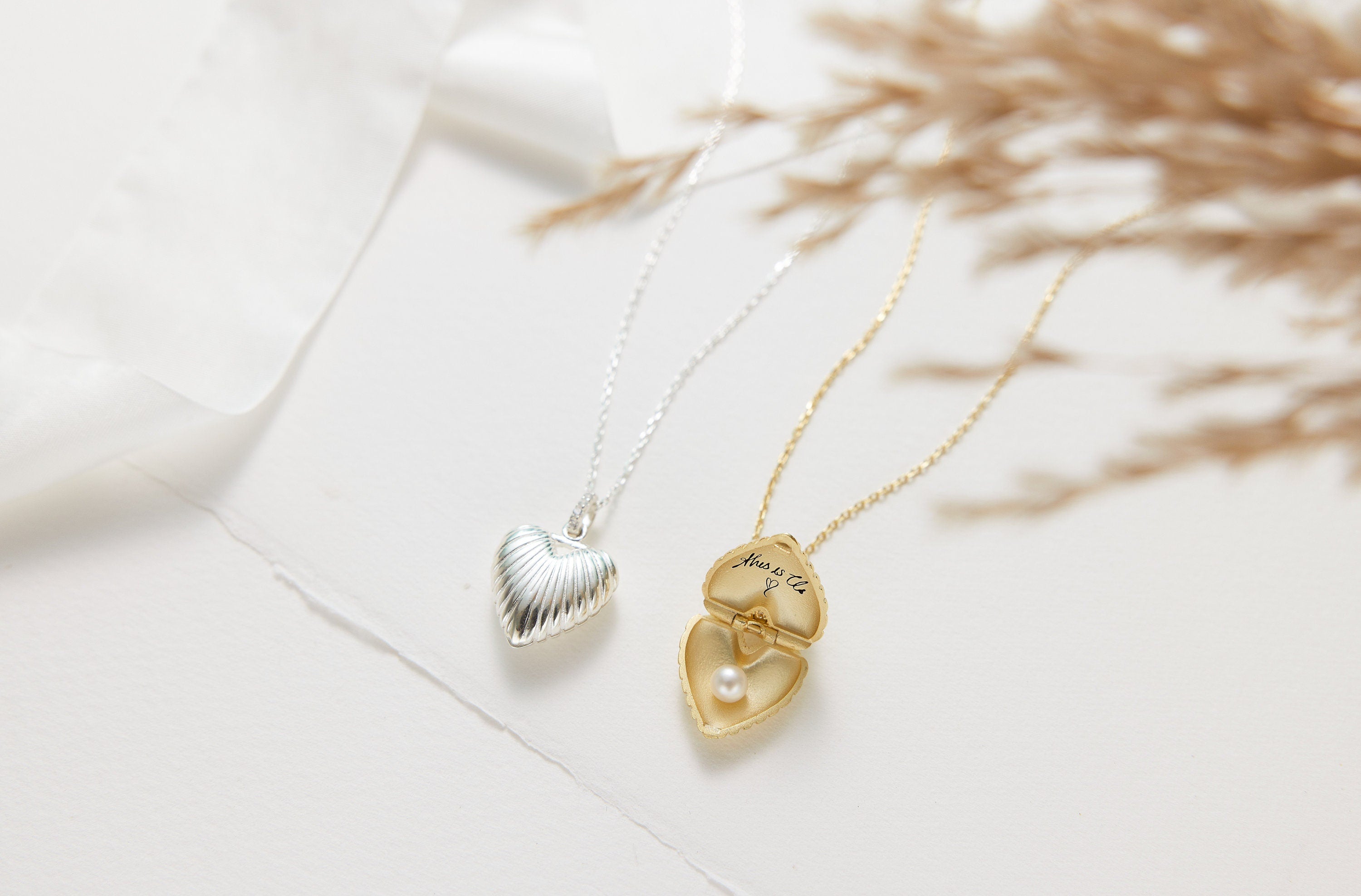 Two heart-shaped necklaces, one gold and one silver, on a light background.