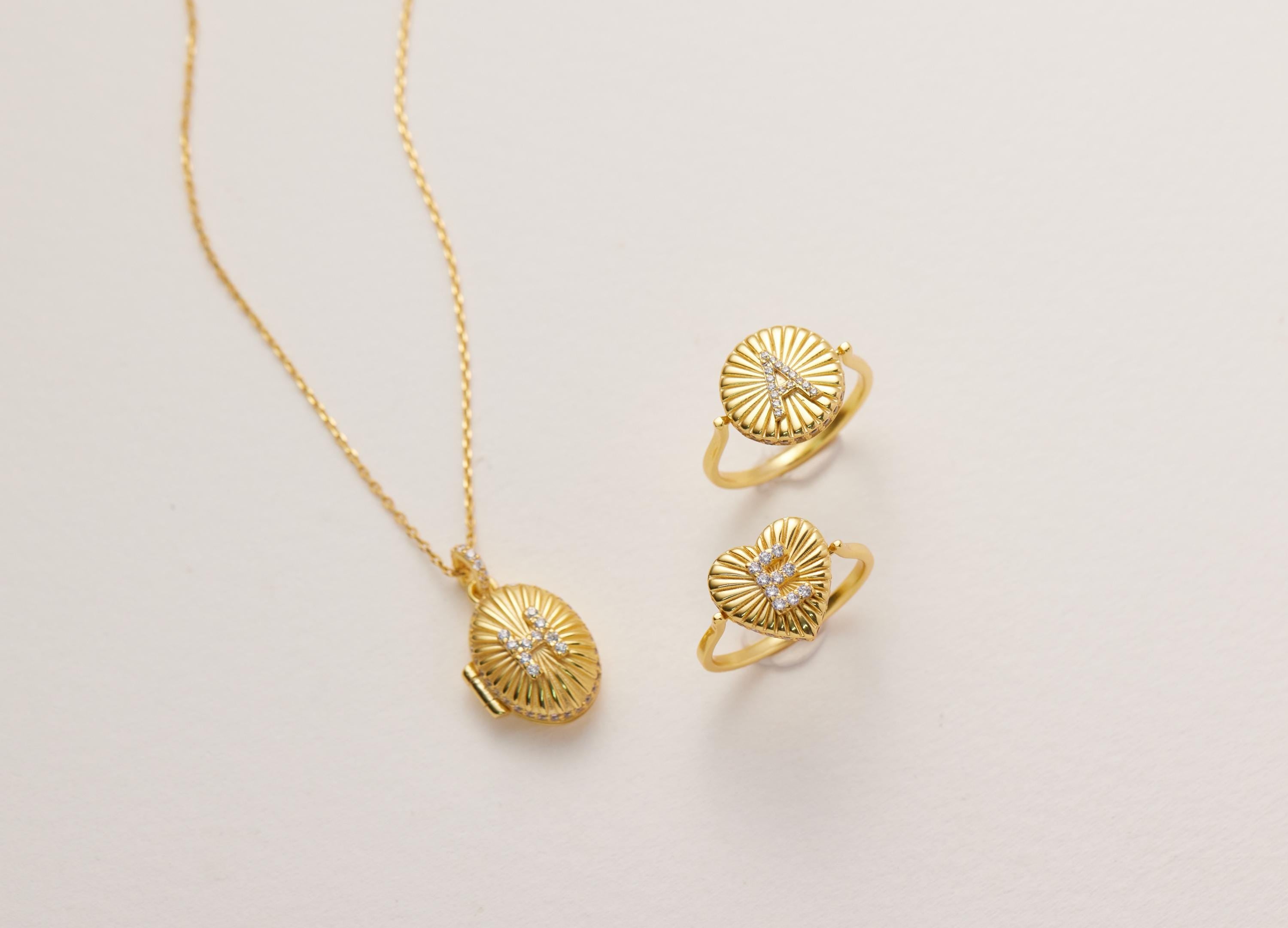 A gold necklace with a pendant and two gold rings with heart-shaped designs are displayed on a white background.