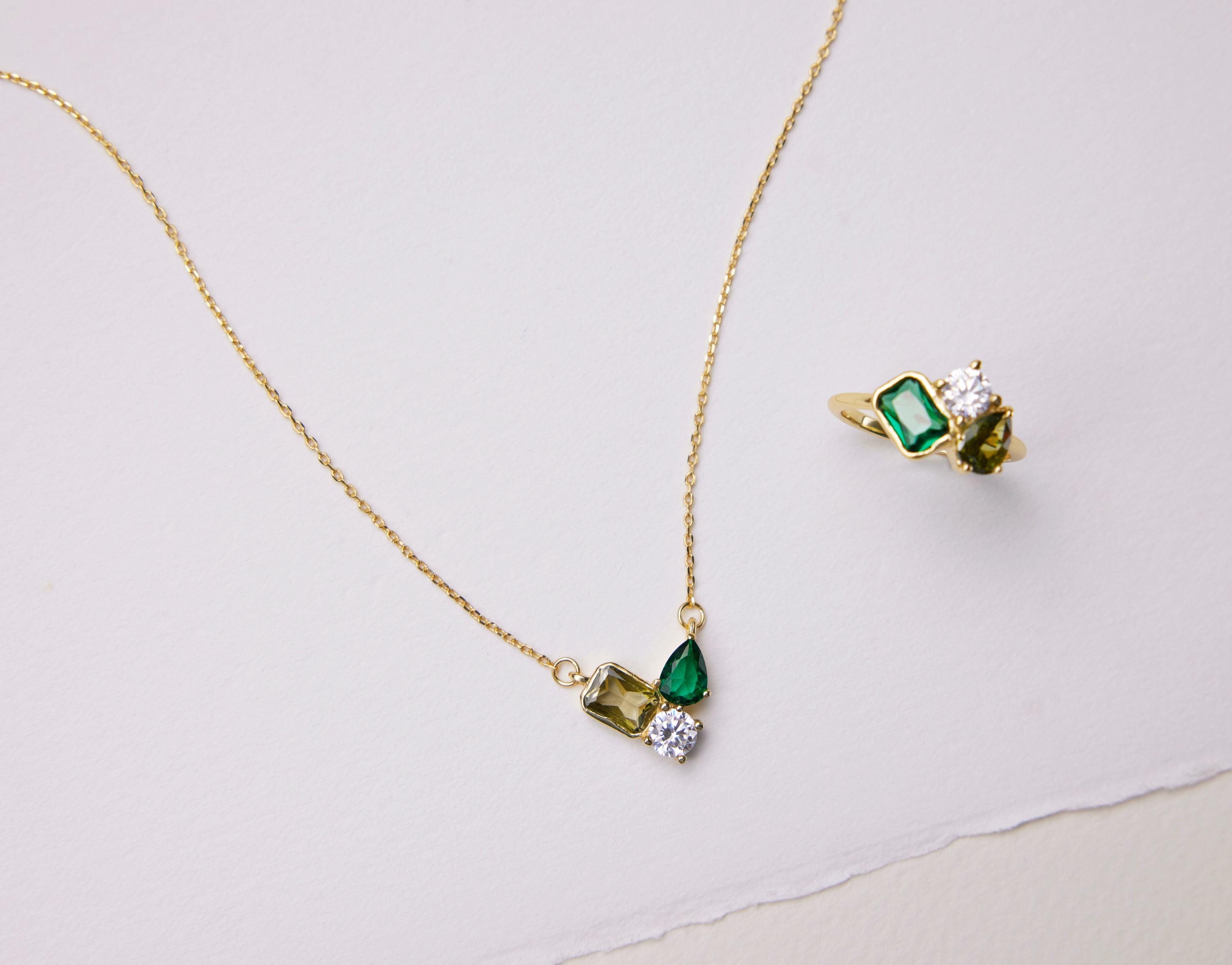 Gold necklace and ring with green gemstones on a light background