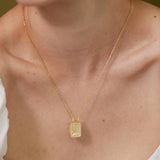 A gold necklace with a square pendant is worn around a woman's neck.