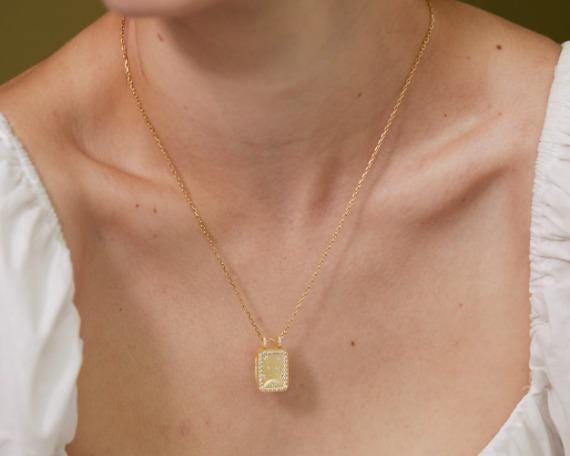 A gold necklace with a square pendant is worn around a woman's neck.