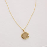 Gold necklace with a round pendant on a light pink background