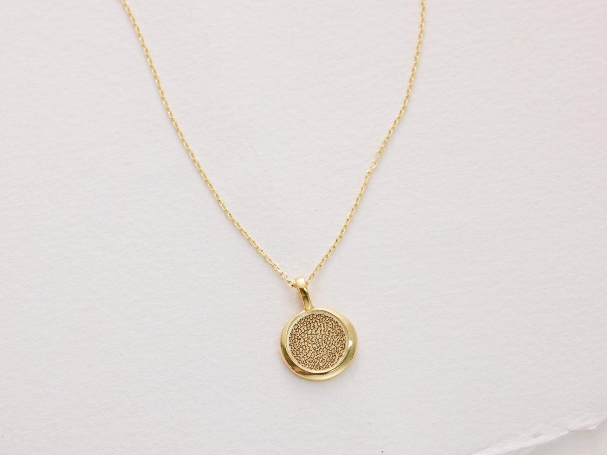 Gold necklace with a round pendant on a light pink background
