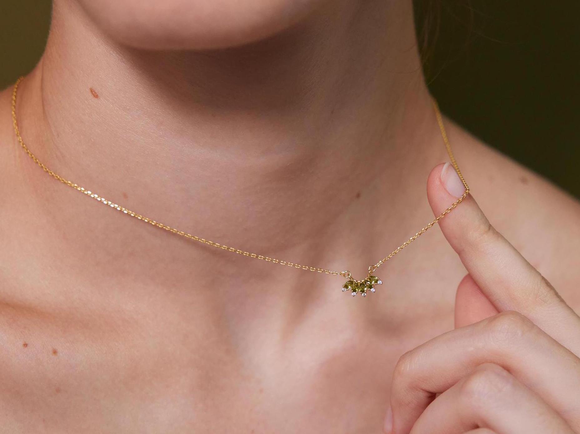 Gold necklace with a green gemstone held by a hand against a blurred background