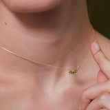 Gold necklace with a green gemstone held by a hand against a blurred background