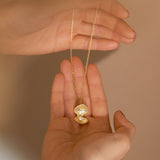 Gold necklace with a heart-shaped pendant held between two hands against a beige background