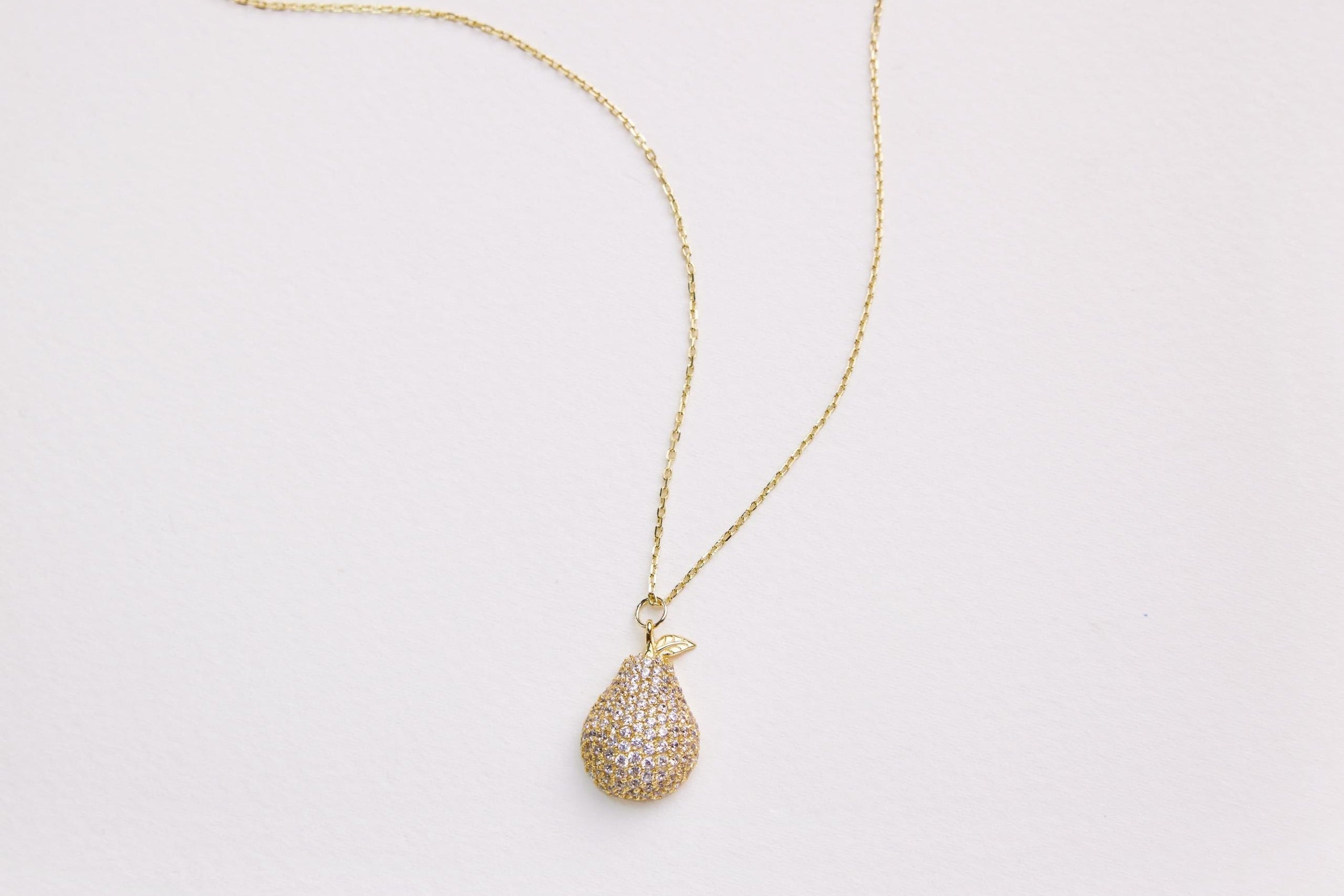 Gold necklace with a teardrop-shaped pendant on a light gray background