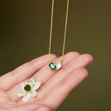 Gold necklace with green gemstone held in a hand against a brown background
