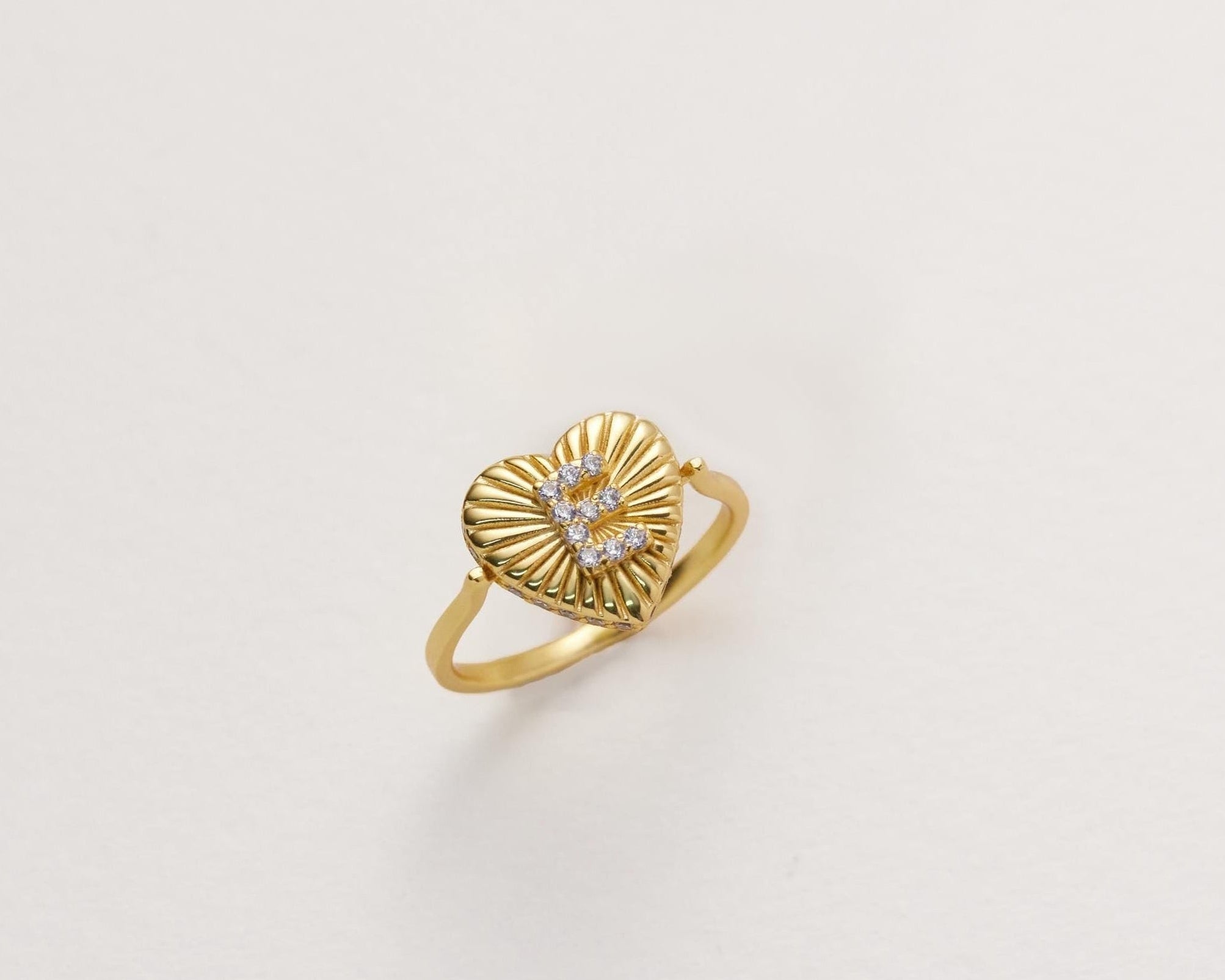 A gold ring with a heart-shaped design and a letter "E" inside it.