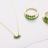 Gold necklace and earrings with green gemstones on a light gray background