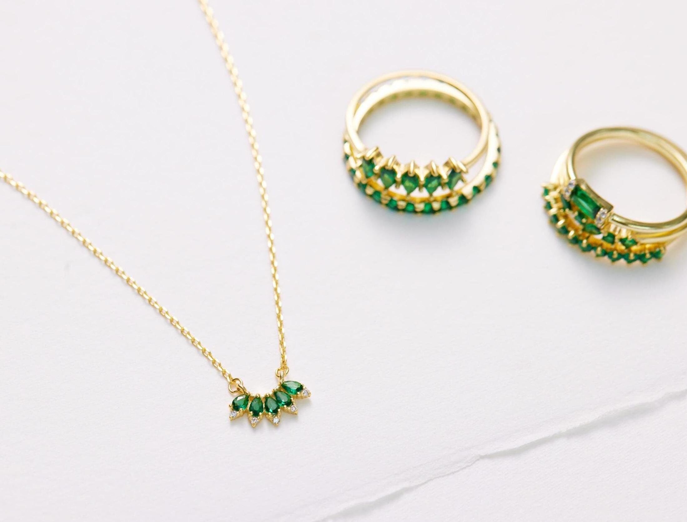Gold necklace and earrings with green gemstones on a light gray background
