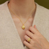 A close-up view of a person's neck and hand wearing a gold necklace and ring.
