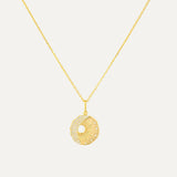 Gold necklace with a round pendant on a light gray background