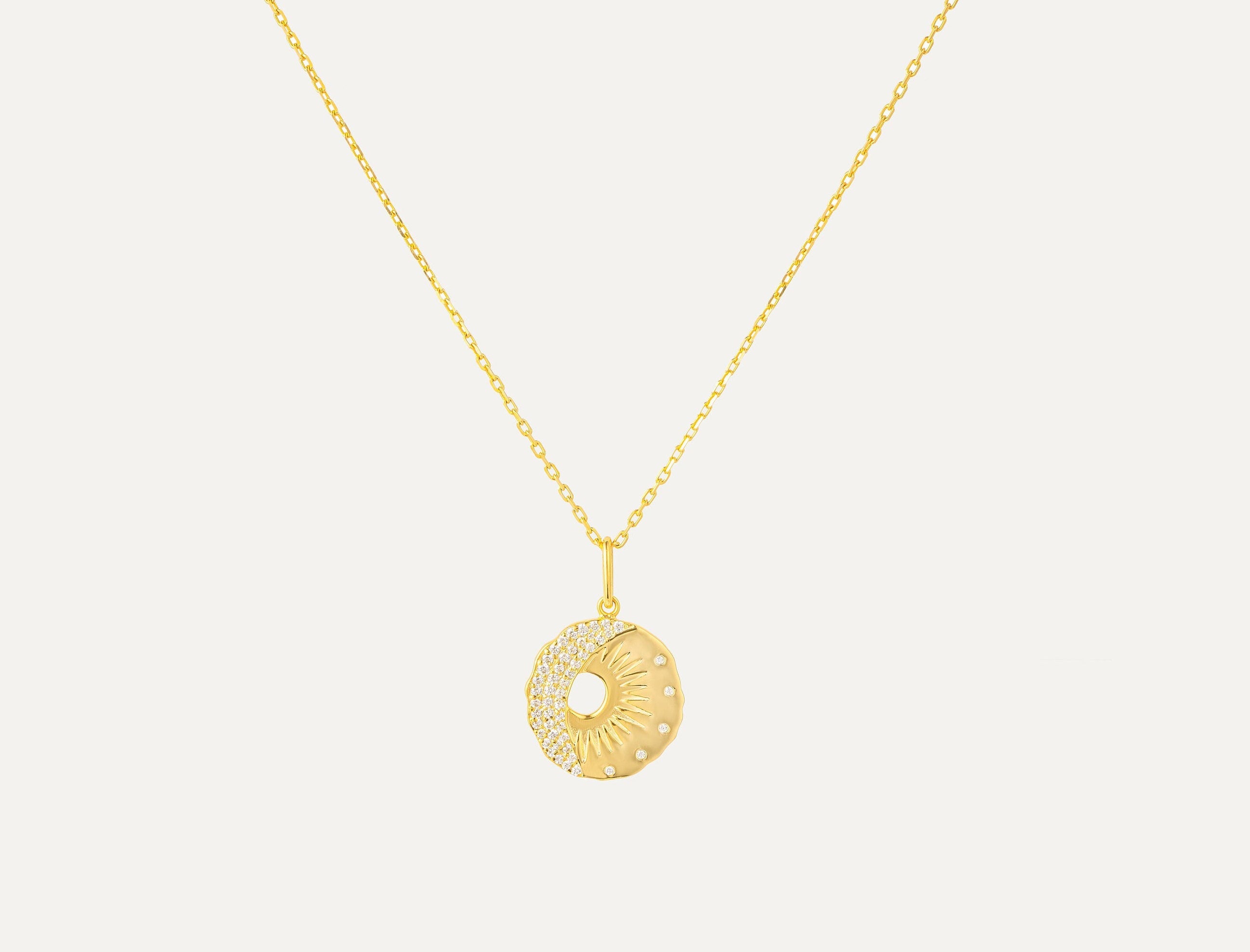 Gold necklace with a round pendant on a light gray background