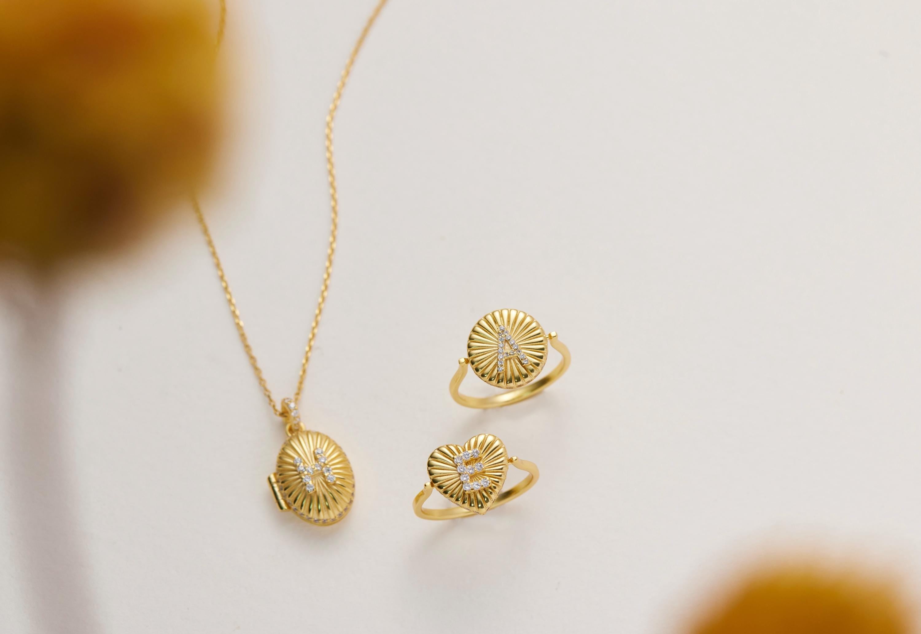 a necklace, two rings, and a locket pendant, all made of gold and displayed on a white background.