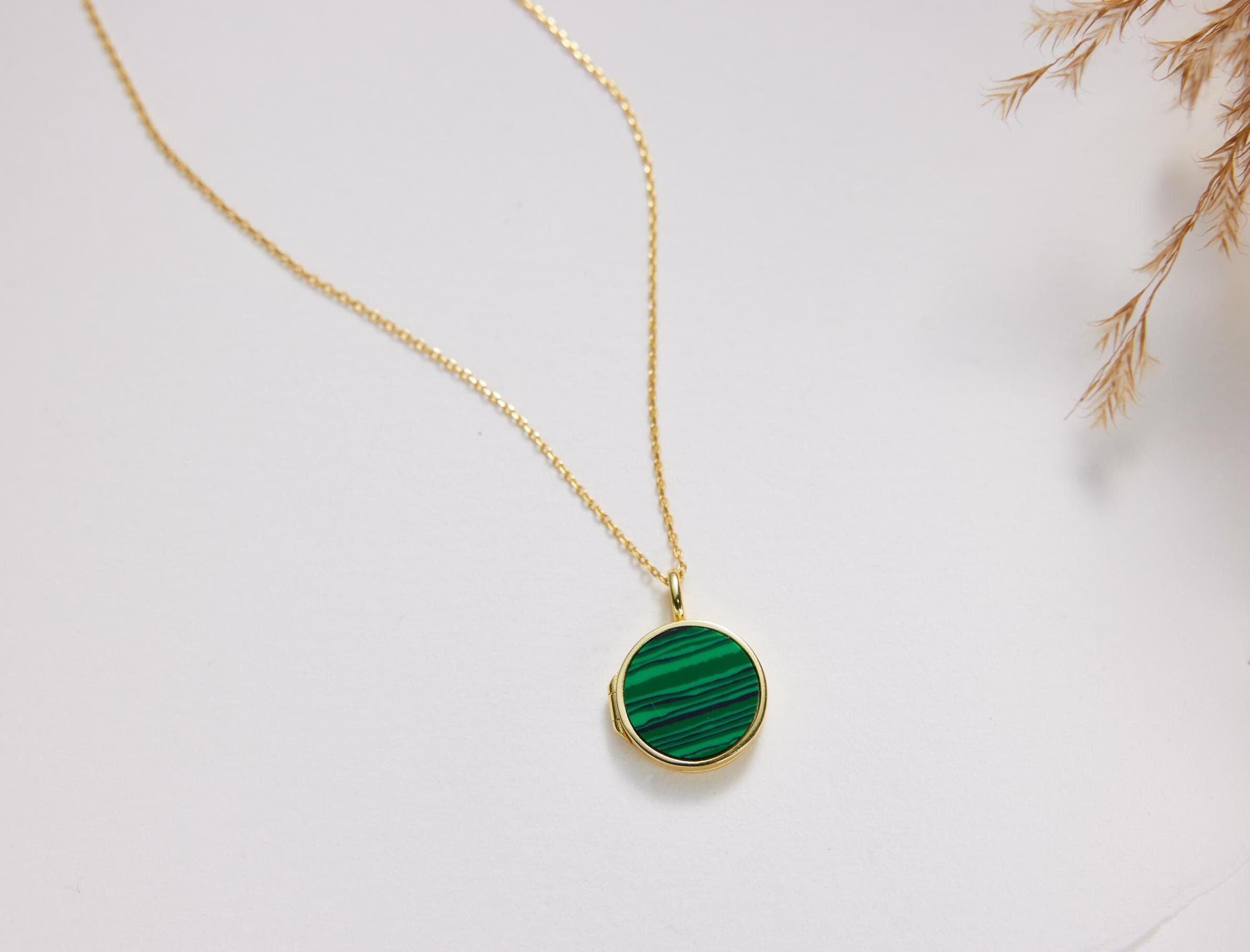 A gold necklace with a round green gemstone pendant is displayed against a white background.